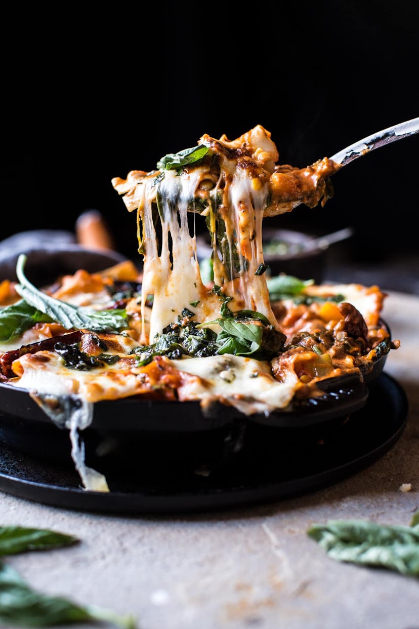 Iron skillet full of vegetarian skillet lasagna with a fork pulling out a chunk and hot cheese strin...