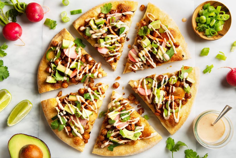Pizza cut into six slices with avocados, lime slices, radishes, green onions, and a special sauce su...