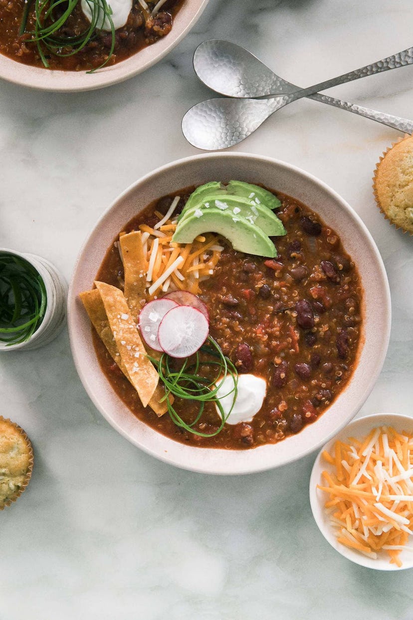 Bowl of vegan chili with avocado and tortilla chip garnishes on a counter top