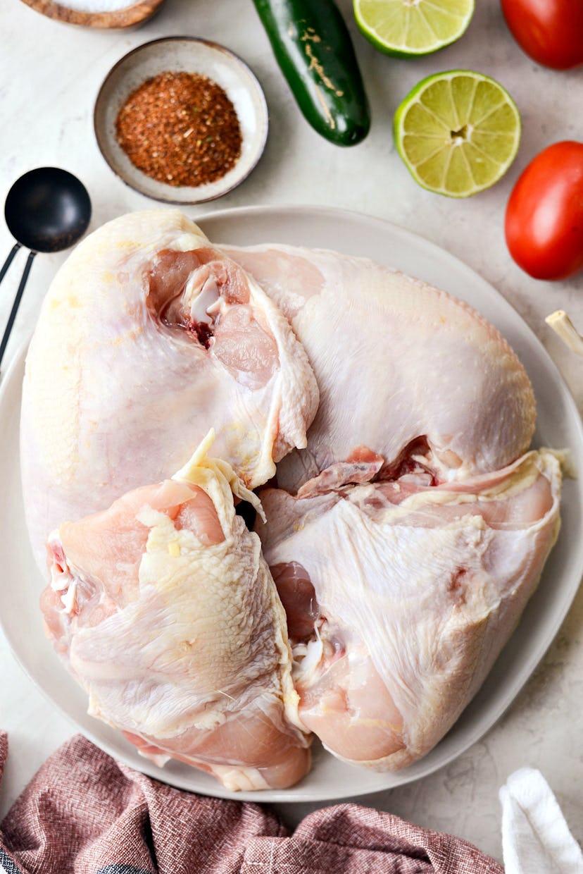 An image of raw chicken surrounded by herbs and spices. 