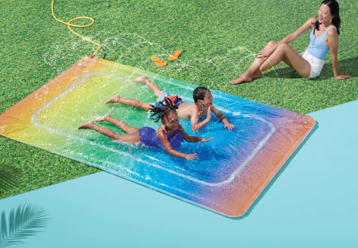 A picture of children sliding on a rainbow inflatable water slide.