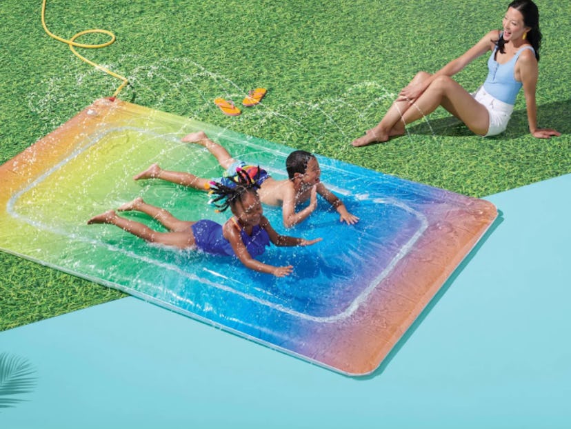 A picture of children sliding on a rainbow inflatable water slide.