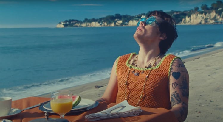 Harry Styles sits at a dining table on the beach in the music video for "Watermelon Sugar."