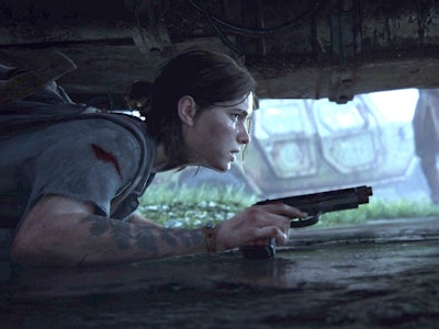 Ellie crouches beneath a car to evade enemies in 'The Last of Us Part II,' out June 19.