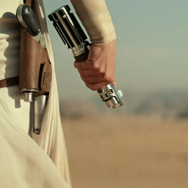Unactivated lightsaber held by a hand in the desert