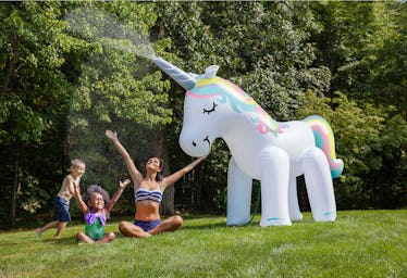 A young family sits in their backyard and plays under a giant unicorn sprinkler.