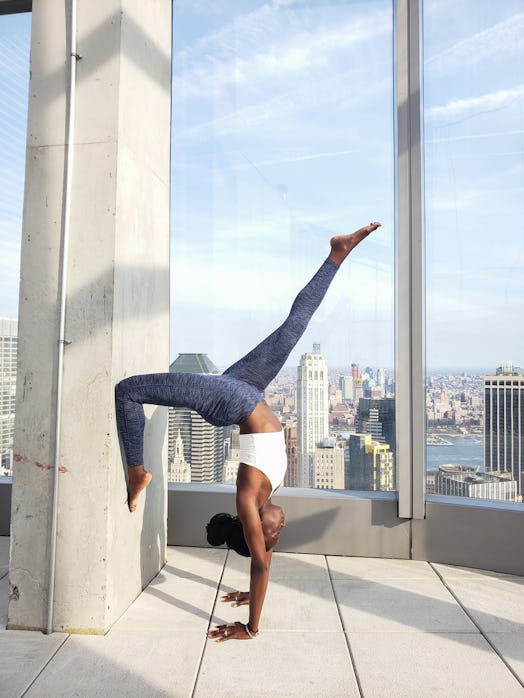 A woman in yoga apparel does a handstand on a rooftop on a sunny day.