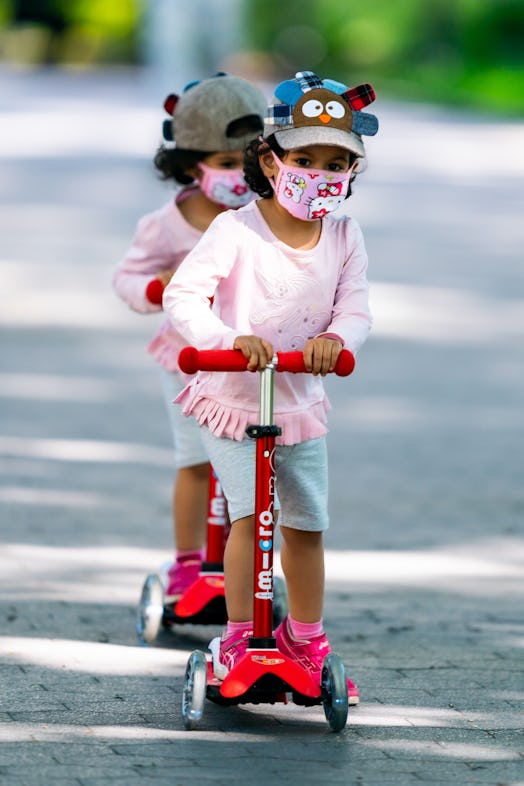 Two girls wear identical protective face masks and outfits on scooters in Washington Square Park dur...