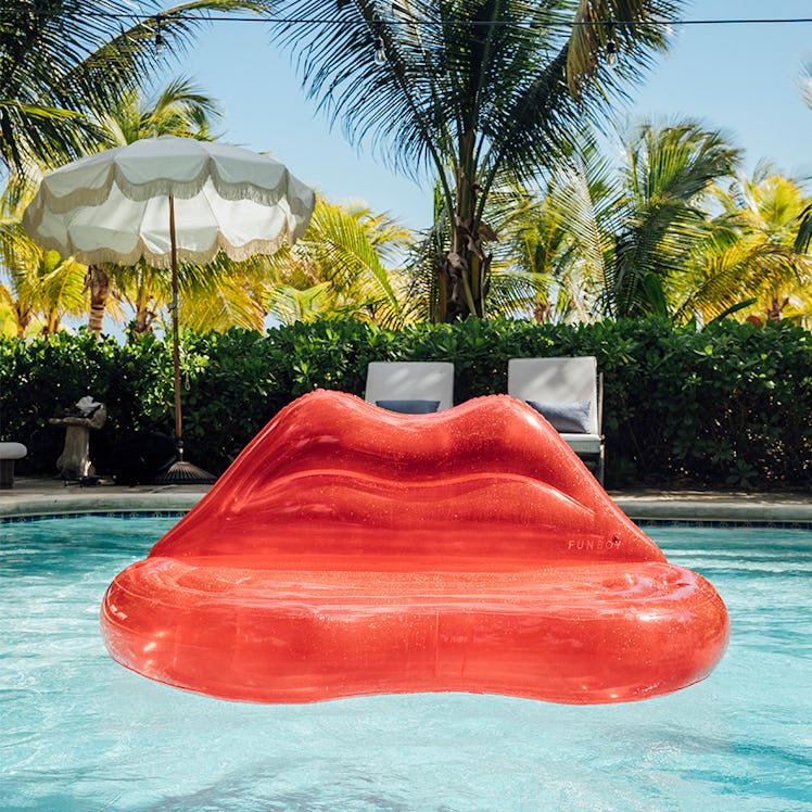 A clear red lips couch inflatable sits in a pool on a summer day. 