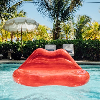 A clear red lips couch inflatable sits in a pool on a summer day. 