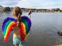 A girl in rainbow wings holds a flag