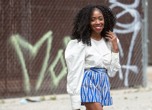 A curly girl wearing a white shirt with puffer sleeves and blue patterned shorts.