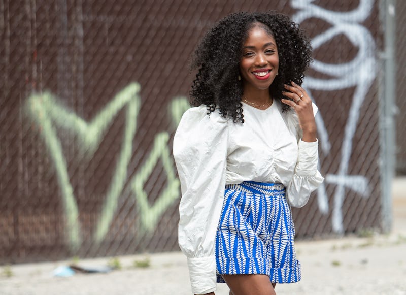 A curly girl wearing a white shirt with puffer sleeves and blue patterned shorts.