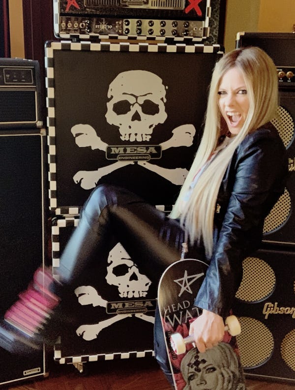 Avril Lavigne taking a photo in a leather jacket and leather pants in the studio with a skateboard. 