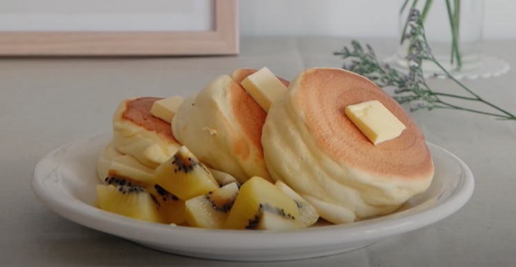 Three Japanese soufflé pancakes are on a plate with butter on top and fruit on the side.