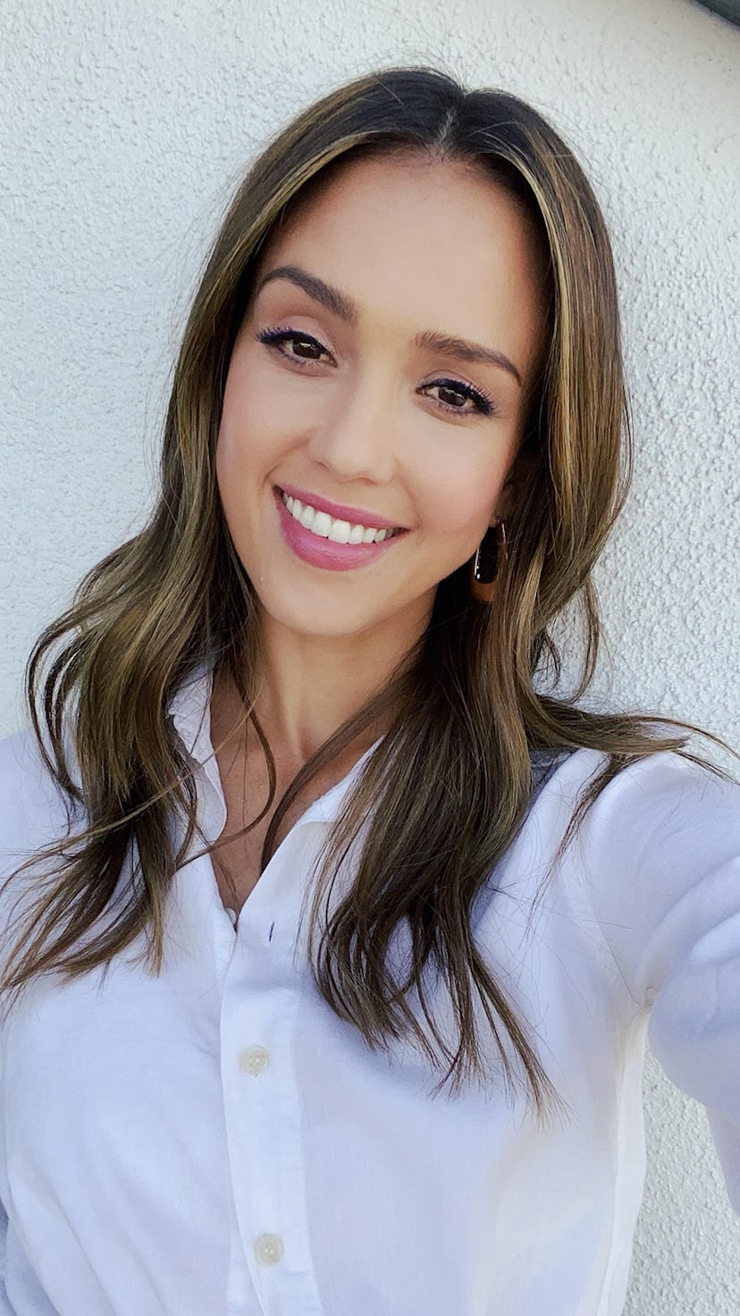 Jessica Alba beaming in a white shirt, in the sunshine outside her home.