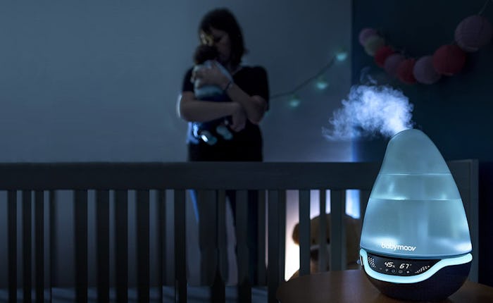A mother holding a child in a dark room with a glowing humidifier in the baby's nursery