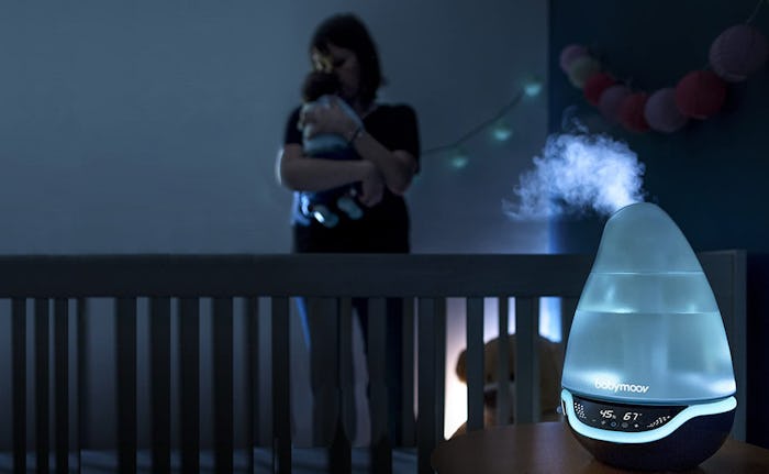 A mother holding a child in a dark room with a glowing humidifier in the baby's nursery