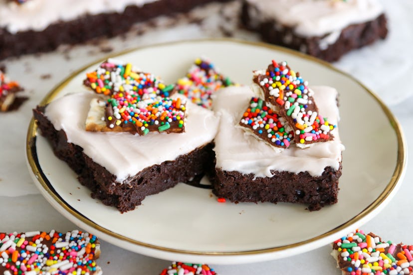 Dark chocolate colored brownies topped in white frosting and sprinkles.