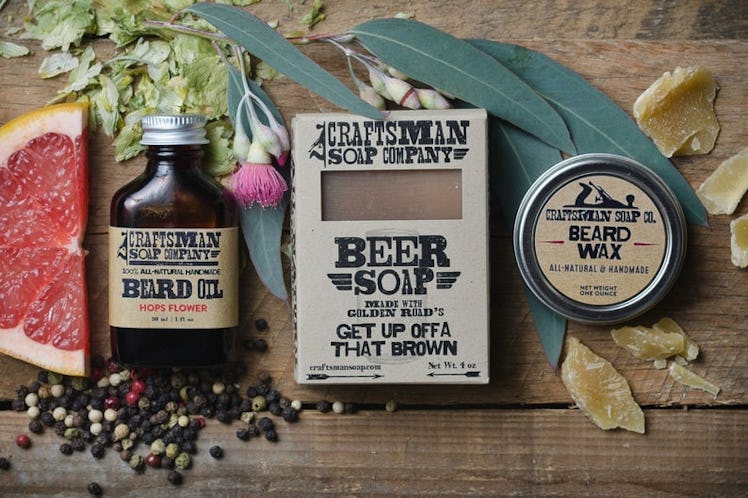 Beard oil, soap, and beard wax are placed on a table next to a slice of grapefruit and flowers in a ...