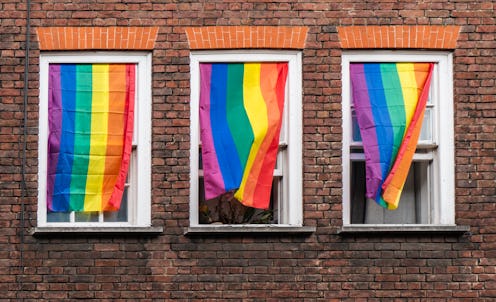 Three windows in the middle of a brick wall, covered with rainbow LGBT flags