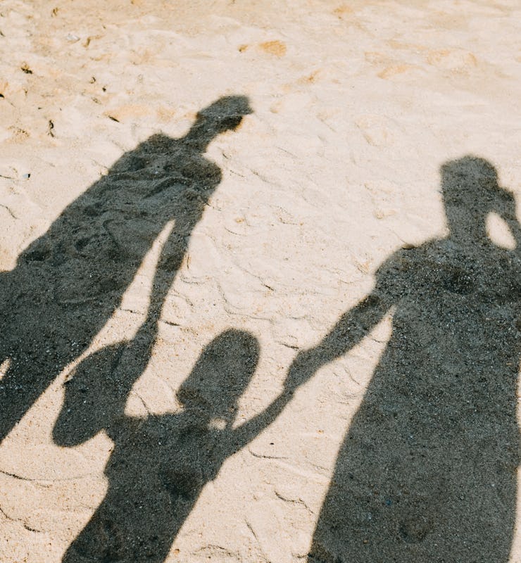 The shadows of two parents and a child in the middle holding hand on a sandy surface