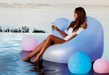 A woman sits on a glow pool float with a glass of wine in her hand. 