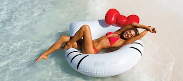 A woman lays out on a Hello Kitty pool float by the water at the beach. 