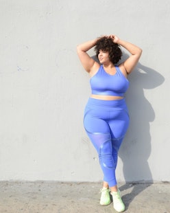 A model posing while wearing blue plus-size leggings that stay up all day and a matching blue sports...