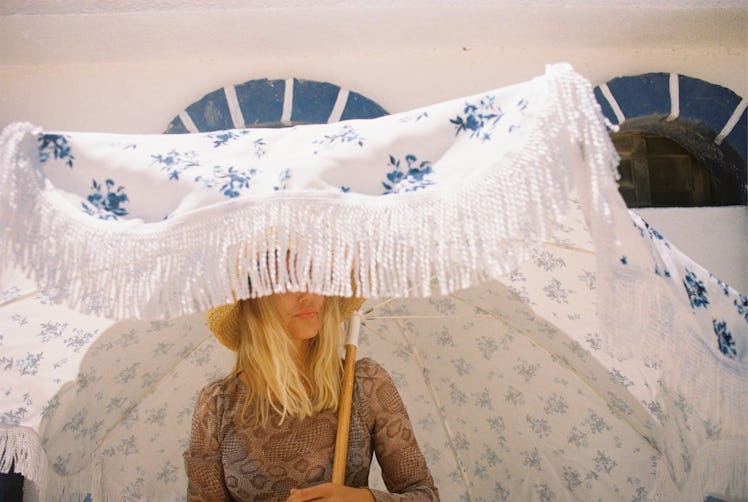 A woman stands under a giant outdoor umbrella in the summer. 