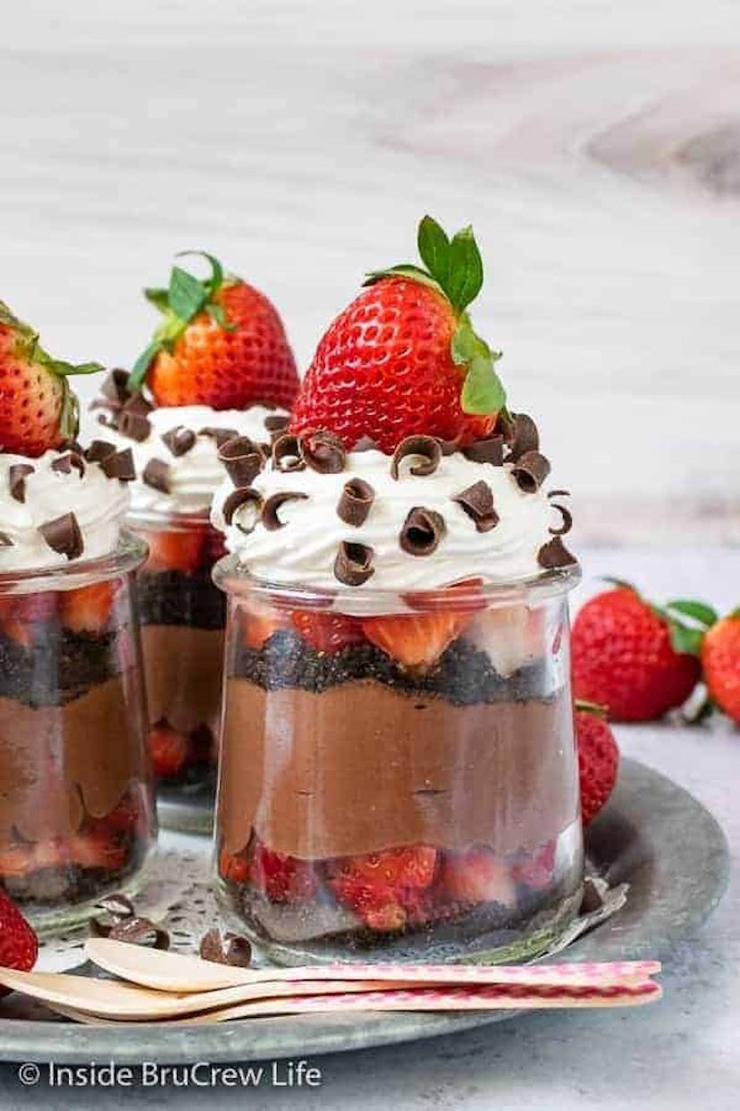 Glasses full of whipped chocolate cheesecake and sliced strawberries topped with whipped cream and c...