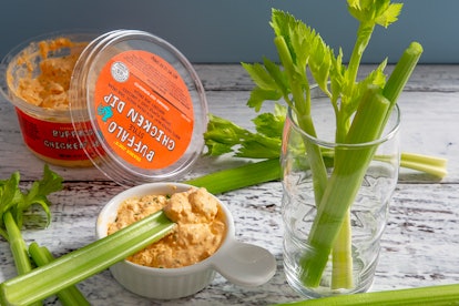 The buffalo-style chicken dip from Trader Joe's sits on a table surrounded by celery.