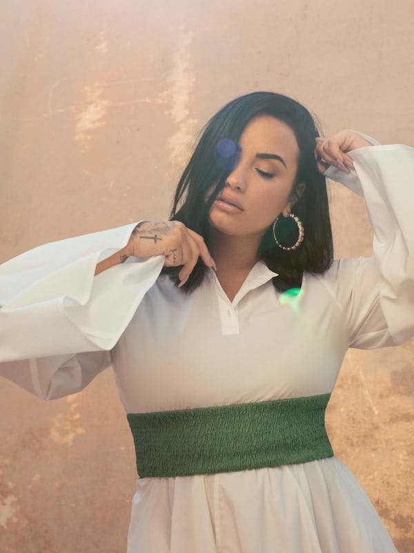 Demi Lovato posing in a white  Net-A-Porter dress with a green belt, Jennifer Fisher ring and Lana J...