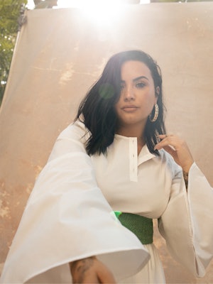 Demi Lovato posing in a white  Net-A-Porter dress with a green belt, Jennifer Fisher ring and Lana J...