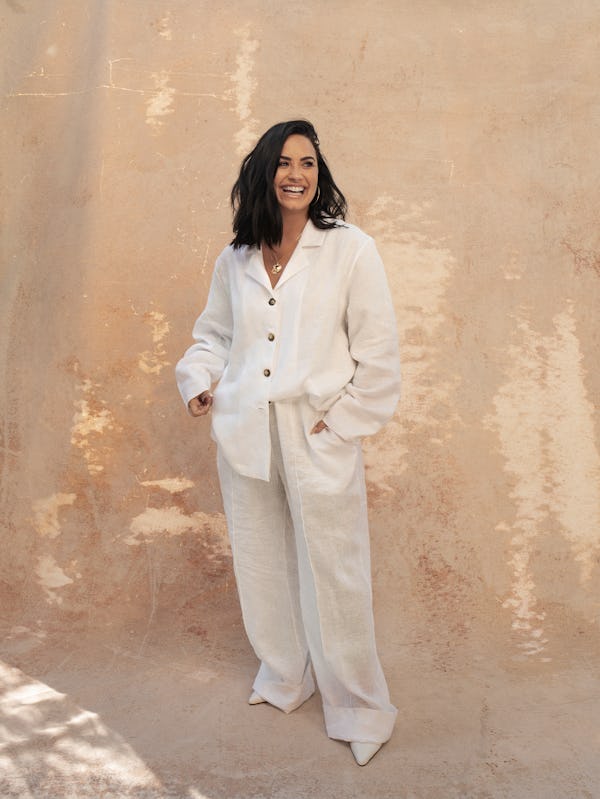 Demi laughing in a white button-up with long sleeves and buttons and in baggy white pants