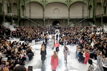 A semi-aerial shot of a group of models walking on a white surface runway with a large audience for ...