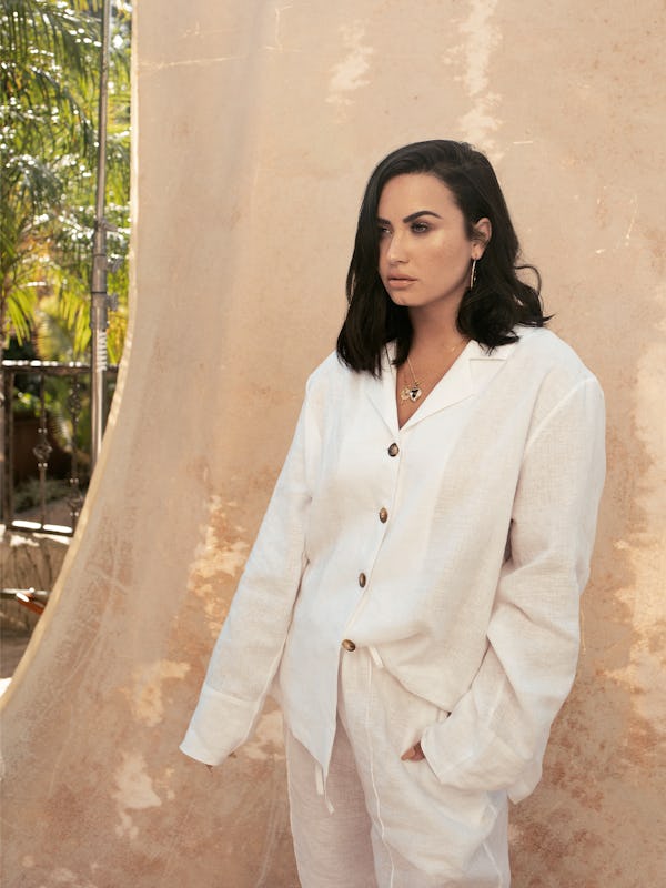 Lovato standing in a white button-up with long sleeves and buttons and in baggy white pants