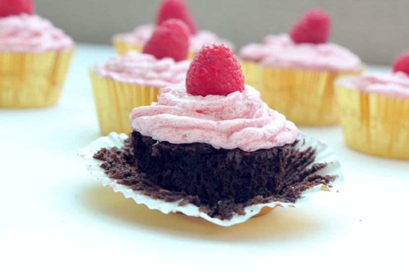 Dark chocolate cupcakes with a fluffy pink frosting, topped with a raspberry, in a gold foil wrapper...