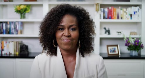 Michelle Obama's in a white top in front of her bookshelves