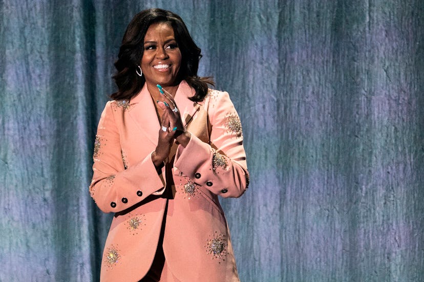 Michelle Obama's in a salmon colored jacket on stage receiving applause 