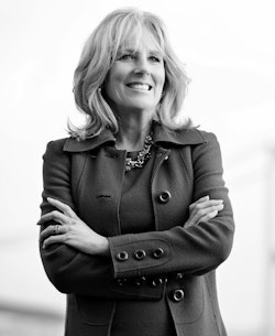 Jill Biden standing with her arms crossed in a formal dress and a long coat