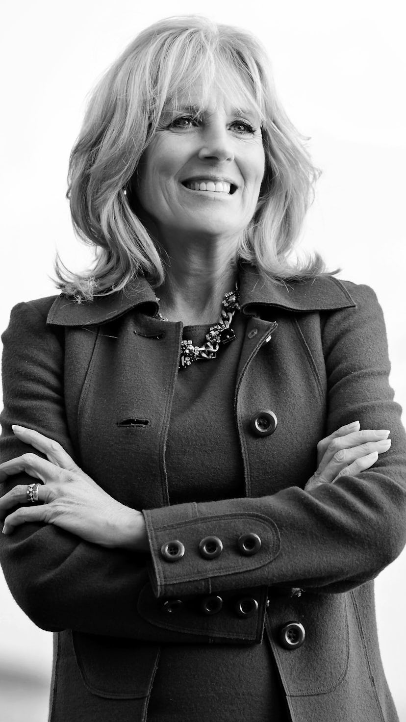 Jill Biden standing with her arms crossed in a formal dress and a long coat