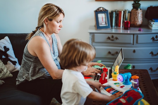 mom and toddler son sitting on couch, mom working on computer