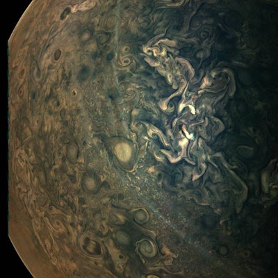 An aerial view of Jupiter's surface in dark green and brown shades