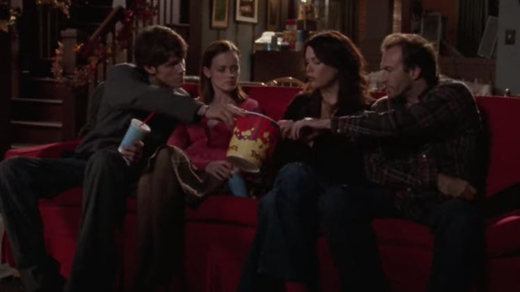 Dean hands Luke a bucket of popcorn at the movies in 'Gilmore Girls.'