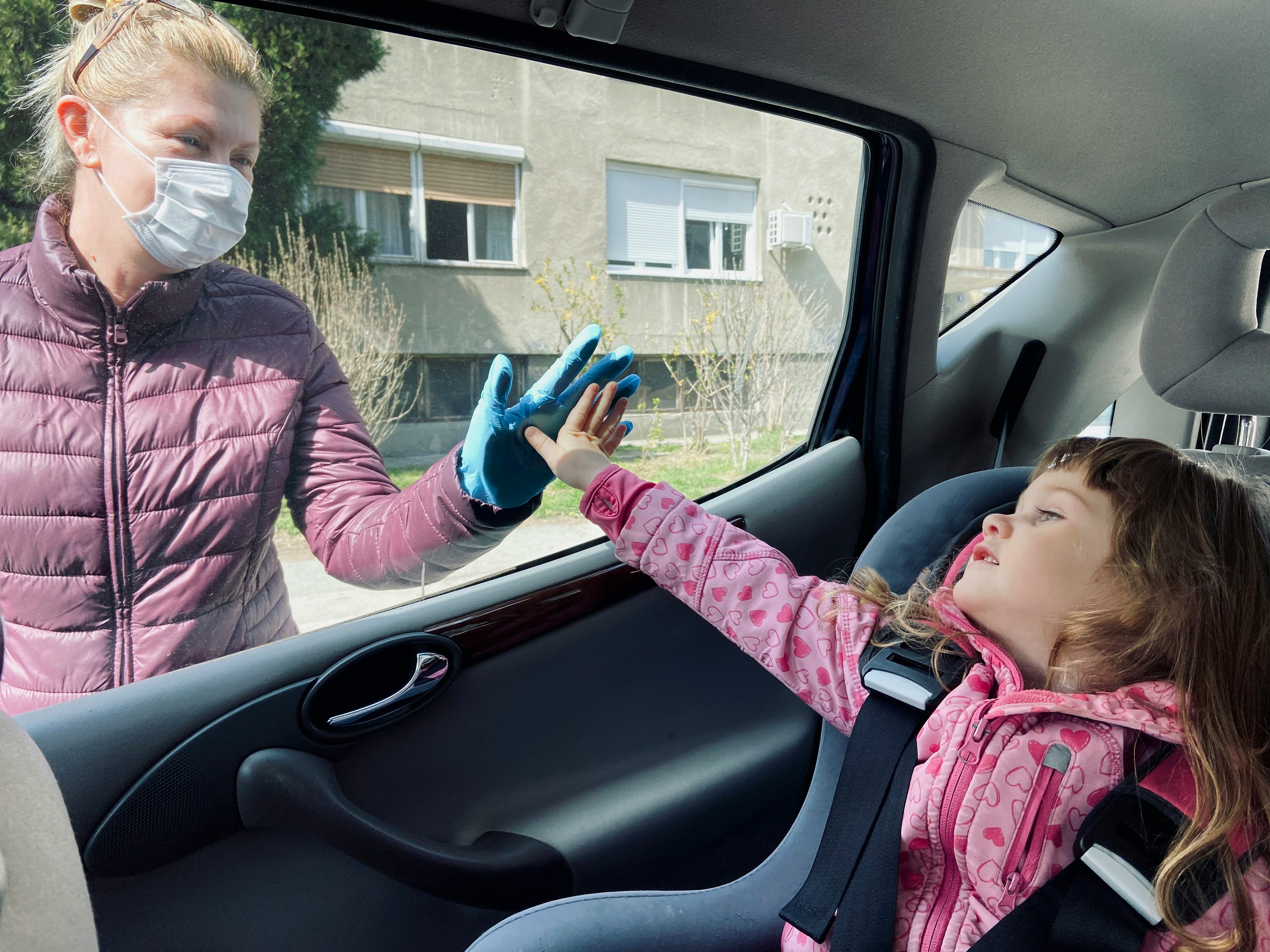 A grandmother and grandchild touch hands on either side of a car window
