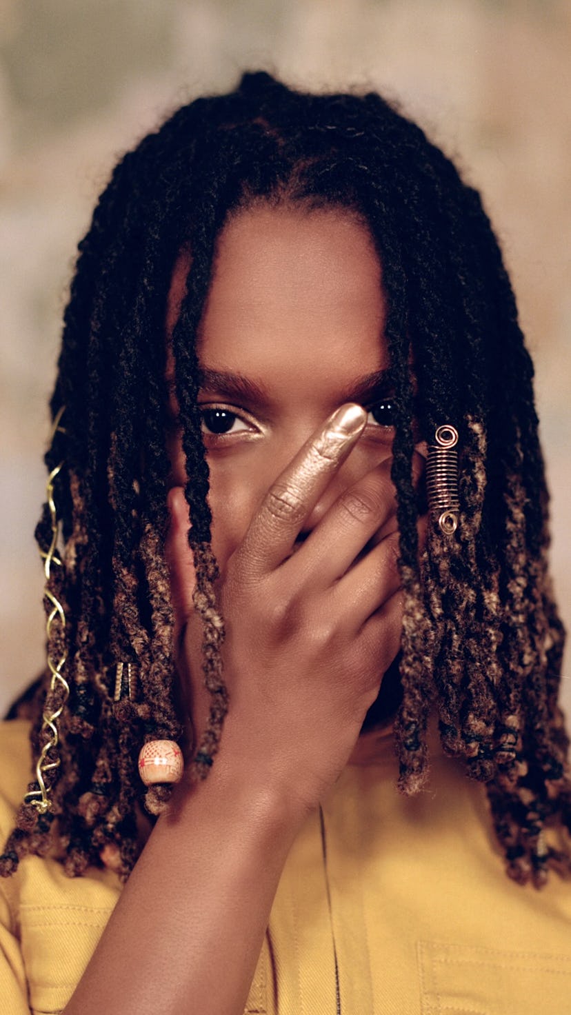 Koffee stands with her hand over her face.
