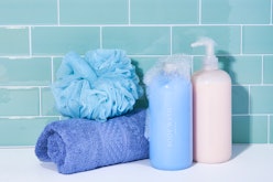 Two shampoo bottles, a blue towel, and a blue hair sponge stacked next to each other