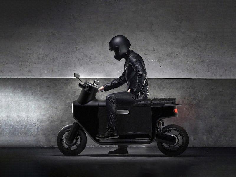 A person wearing all black sitting on a black scooter.
