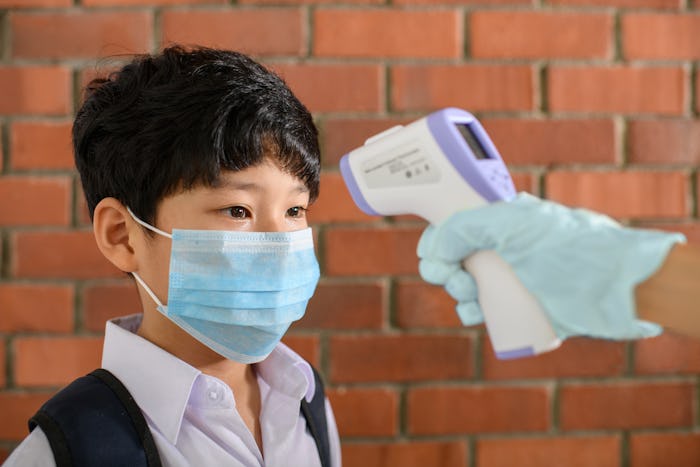 boy with face mask and backpack getting his forehead temperature taken